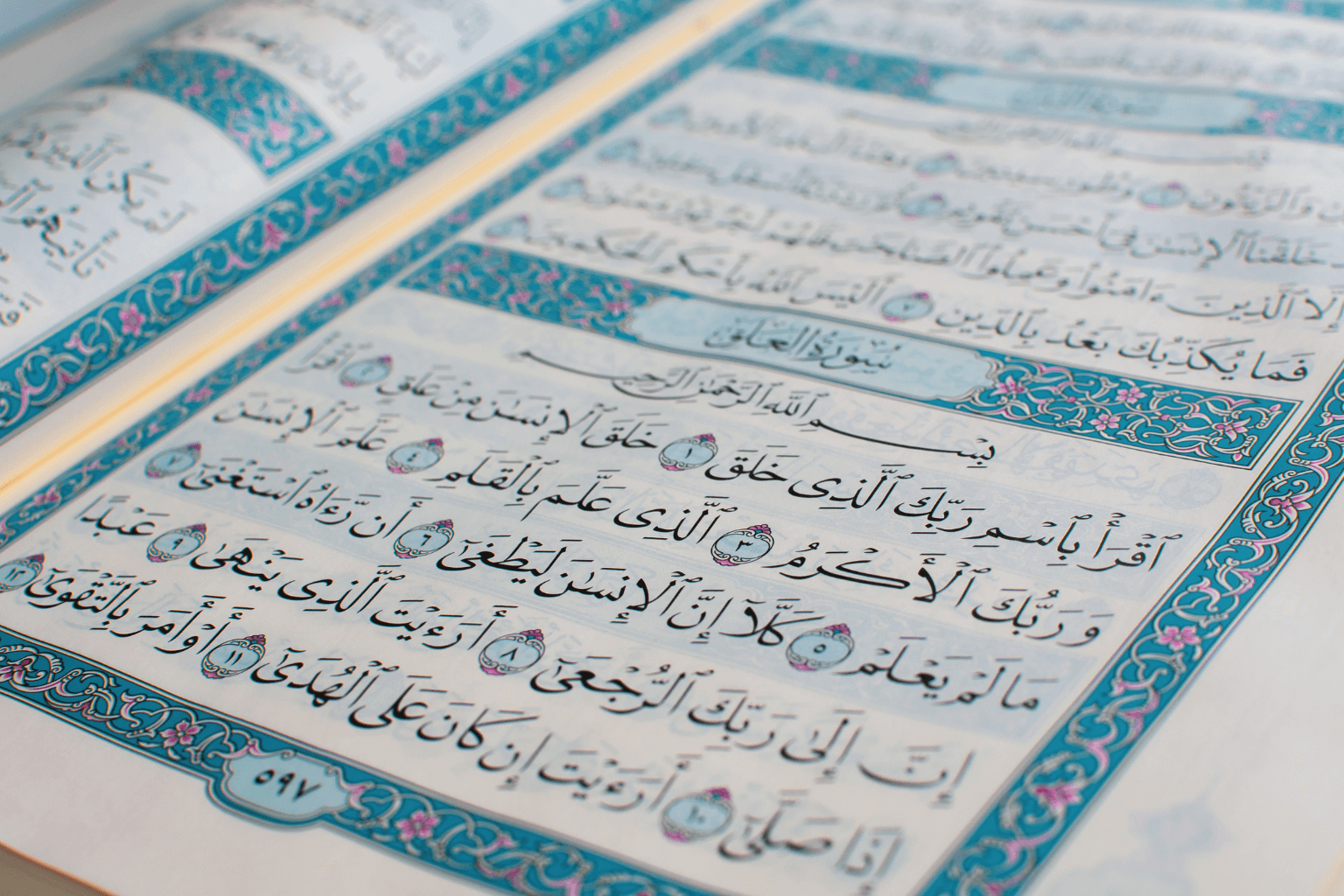Page du Coran ouverte sur la sourate Al-‘Alaq avec une calligraphie arabe élégante et des bordures décoratives bleues